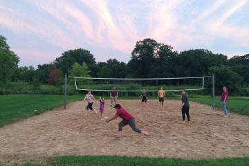 group of adults playing sand volleyball, one adult ready to serve the volleyball